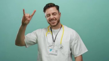 Steteskop takmış genç bir adam yeşil arka plana karşı el hareketi yapıyor. Sıradan ve dostane bir tavır sergiliyor..