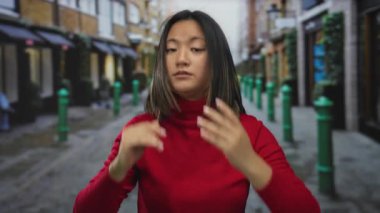 Kırmızılı kadın şehir sokaklarında sükunet için jestler yapıyor, bir şehir ortamında huzur ve yansıma anı yakalıyor..