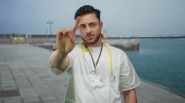 Steteskoplu beyaz önlüklü genç sakallı doktor deniz kenarında okyanus manzaralı gezinti yapmaz.