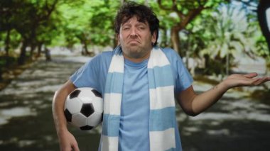 Parkta futbol oynayan İspanyol bir adam, güneşli yeşil bir yolda dikilirken belirsizliğini ifade eder..