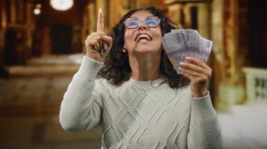 Kilisede elinde Rupiah banknotları tutan orta yaşlı bir kadın heyecanını dile getiriyor ve yukarıya doğru işaret ediyor. Mali güç ve kültürel bağlam tasvir ediyor..