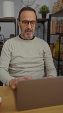 Ofisteki İspanyol adam dizüstü bilgisayar kullanırken stresli görünüyor, elleri ve gözleri kapalı, arka planda ofis malzemeleri ve raflarla çevrili..