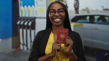 Dışardaki benzin istasyonunda gülümseyen ve elinde Fransız pasaportu olan bir kadın, arka planda pompaları olan bir araba, seyahat hazırlığı ve çeşitliliği iletiyor..