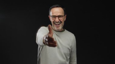 Sakallı ve gözlüklü gülümseyen adam siyah arka planda el sıkışma, dostluk ve güven iletiyor.