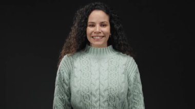 Samimi süveter giyen İspanyol kadın, izole edilmiş siyah arkaplan duvarına el hareketi yaparak dostça ifadeyi yakalıyor..