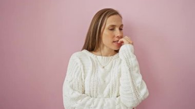 Kazaklı genç bir kadın stresli ve endişeli, gergin bir şekilde elleri dudaklarının üzerinde pembe arka plana yaslanıyor, duygusal hassasiyet ve endişe sorununu vurguluyor.