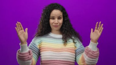 Kıvırcık saçlı, elleri mor arkaplan üzerinde hareketli pastel renkli gökkuşağı süveter giyen kadın.