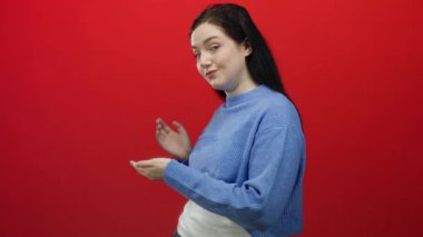 Mavi kazaklı kadın, canlı kırmızı arkaplana karşı yaratıcı bir şekilde el kol hareketi yapıyor, zarif ve duygularını esmer saçlı, kendine güvenen bir duruşu, harmanlayan güzel ve modern moda ile ifade ediyor..