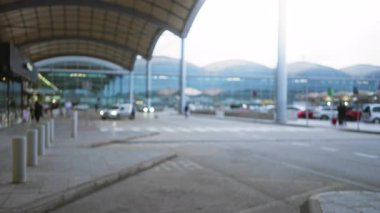 Kalabalık bir havaalanı terminalinin bulanık görüntüsü ve arka planda odakları kesilmiş insanlar ve araçlar gün ışığında.