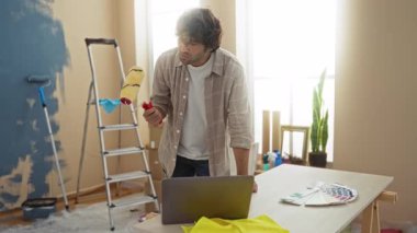 Evde resim yapan genç bir adam oturma odasını ararken masada resim aletleri ve dizüstü bilgisayarlar vardı..