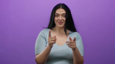 Genç, kıvrımlı bir kadın, açık mavi bir bluz giyen ve dostça iletişimi ifade eden canlı mor bir arka plana davetkar bir şekilde el kol hareketi yapar..