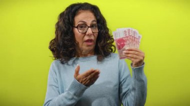 Icelandic Krona 'nın banknotlarını elinde tutan kadın, parlak sarı bir arkaplana karşı esprili bir şekilde, açık yürekli ve izole bir sahnede finansal kavramları sergiliyor..