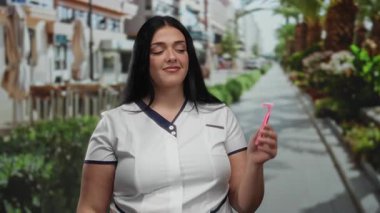 Güneşli bir günde palmiye ağaçlarıyla kaplı bir caddede pembe jilet tutan kadın, şehir hayatı ve kendine güveni somutlaştırıyor..