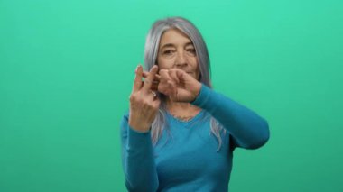 İzole edilmiş yeşil arka plan duvarına işaret eden gri saçlı yaşlı kadın modern iletişim ve sosyal etkileşimi somutlaştırıyor..