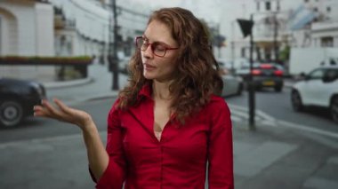 Kırmızı saçlı ve gözlüklü bir kadın Londra 'nın işlek bir caddesinde duruyor. Trafiğin ortasında düşünceli bir ifadeyle elini uzatıyor..