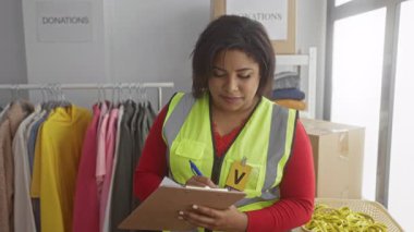 Hayır kurumu bağış merkezinde iç mekanda gönüllü iş ve organizasyon olduğunu belirten giysiler ve kutularla dolu yansıtıcı yelek giyen bir kadın..