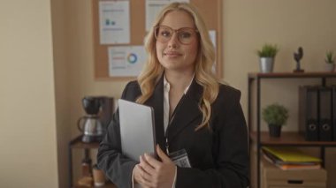 Modern ofiste gülümseyen bir kadın elinde tabletle, arka planda iç mekan bitkileri ve ofis malzemeleriyle profesyonelliği ve arkadaşlığı aktarıyor..