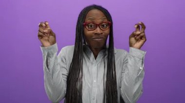 Mor duvara karşı kıvırcık saçlı ve gözlüklü el hareketleri yapan bir kadın neşeli bir ifade ve tavır sergiliyor..