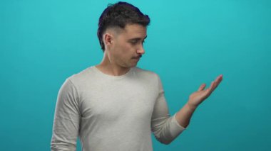 Latin kökenli genç bir adam, mavi izole edilmiş arka plana karşı elleri açık bir şey sunuyor. Günlük kıyafetler giyiyor..