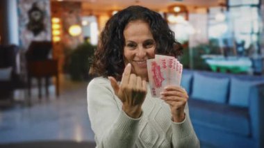 Otel resepsiyonunda elinde Çin banknotları tutan kadın gülümseyen yüz ifadesi ve konukseverlik bağlamında bir jest yapıyor..