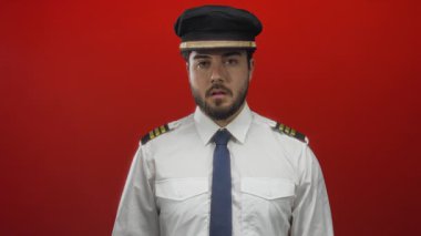 Üniformalı, sakallı genç İspanyol pilot canlı kırmızı arka plana karşı, profesyonellik ve havacılık uzmanlığını vurguluyor..