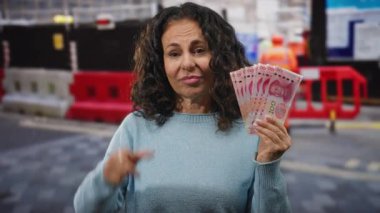 Şehirde orta yaşlı bir kadın Çin Yuan banknotlarını elinde tutarken başarısız bir jest yapıyor ve finansal hayal kırıklığını dile getiriyor..