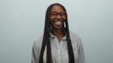 Uzun saçlı ve gözlüklü gülümseyen bir kadın saf beyaz bir duvarın arkasında neşeli bir hareketle izole edilmiş.