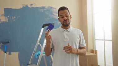 Yeni evin içinde elinde kredi kartı tutan genç bir adam. Üzerinde boya merdiveni karton kutular var. Oturma odasında tefekkür ve karar verme mekanizmasını gösteriyor.