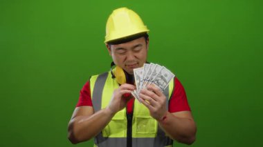 Amerikan dolarlarını tutan Asyalı adam, yeşil arka planda izole edilmiş, baş parmağıyla küçümsediğini ifade ediyor..