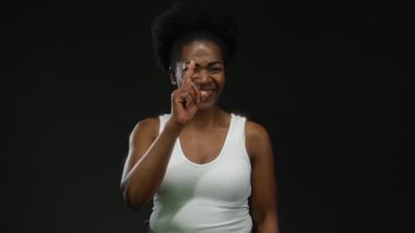 Afro-Amerikan genç bir kadının neşe ve ifadesini yansıtan canlı bir stüdyoda izole edilmiş siyah bir arkaplana güvenle gülümseyen bir kadın..