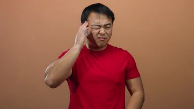 Baş ağrısını ifade eden genç bir adam gözleri kapalı ve elleri kafasında kahverengi arka planda izole edilmiş.