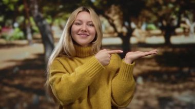 Ağaçlarla çevrili güneşli parkta, sarı süveter giymiş gülümseyen bir kadın, doğa ortamında neşeli bir hava ve dostane bir atmosfer anlamına gelir..