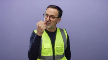 Sarı yelekli İspanyol bir adam öfkesini mor bir duvar arkasına doğru kaldırarak gösteriyor. Olgun bir erkek ifadesinde duygu ve hayal kırıklığını gösteriyor..