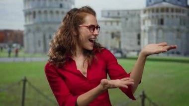 Gülümseyen kadın, İtalya 'da sidik kulesinin yanında elini uzatıyor. Kırmızı tişörtlü, açık havada güneşli bir gün portresi gözlüğü takıyor. Turist çekimleri canlanıyor..