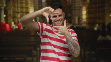 Kilisedeki genç adam çerçeveli elleriyle gülümsüyor. Kilisenin iç tarafında çizgili tişört giyiyor. Gün içinde evde yaratıcılık ve pozitiflik olduğunu gösteriyor..