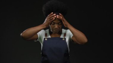 Önlüklü kadın, iş yerindeki stresi vurgulayan siyah arka plana karşı hayal kırıklığı içinde..