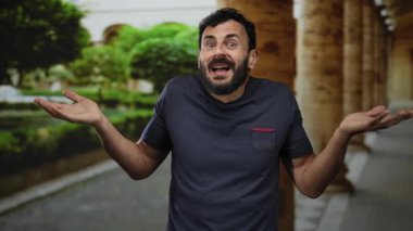 Üniversite kampüsünde sakallı İspanyol bir adam arka planda eski bir mimariyle kafa karışıklığı ya da belirsizliği dile getiriyor..