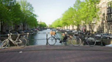 Arka planda Amsterdam 'ın ikonik kanalları ve yemyeşil yemyeşil gölgeli bir atmosfer yaratan bir köprüye parketmiş bisikletler..