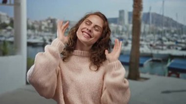 Sahil marinasında rahat bir kazakla gülümseyen bir kadın kayıklar ve palmiye ağaçları ile açık havada açık havada, açık bir gökyüzünün altında huzurlu bir anı yakalıyor..