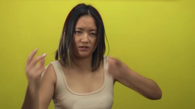 Parlak sarı bir duvara yaslanmış ellerle hayal kırıklığını ifade eden genç bir kadın, kolsuz bir bluz giyiyor, duygularını canlı bir şekilde aktarıyor ve odak noktasını büyütüyor..