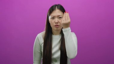 İzole edilmiş pembe arka planda, el hareketleriyle hayal kırıklığını ifade eden, uzun düz saçları olan ve günlük beyaz gömlek giyen bir kadın..