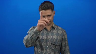 Genç adam kendine güvenen bir tişörtle izole edilmiş mavi bir arkaplanı işaret ederek dikkatleri üzerine çekiyor ve nişan alıyor..