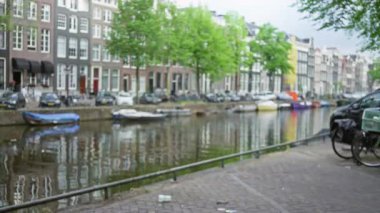 Durgun kentsel bir ortamda, ağaçlık bir cadde boyunca park etmiş arabalar ve bisikletlerle renkli tarihi binalara karşı bulanık bir manzara..