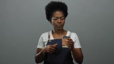 Önlük giymiş bir kadın kahve fincanı tutarken gri arka plana karşı olumlu tavır sergiliyor..