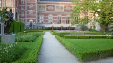 Tarihi bir müze bahçesinin bulanık manzarası. Bir heykel ve yemyeşil çitler baharda sakin bir atmosfer yaratıyor..