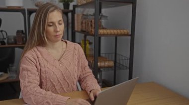 Kadın, rahat ofis ortamında dizüstü bilgisayarla masada meditasyon yapıyor, rahatlamayı gösteriyor ve rafları ve dekorasyonu olan modern bir işyeri ortamında odaklanıyor..