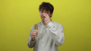 Parlak sarı arka planda dondurma tutan yakışıklı bir adam, kameraya kendinden emin bir şekilde bakıyor, çizgili gömlek giyiyor, arkadaşça bir etkileşim ve yaz keyfi öneriyor.