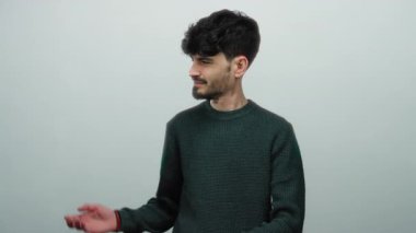 Siyah saçlı ve sakallı genç adam süveter giyiyor, izole edilmiş beyaz bir arka plan üzerinde hareketler yapıyor..