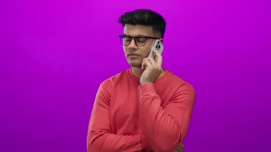 Kırmızı kazaklı yakışıklı adam telefonda canlı pembe arka planla ilgili konuşuyor. Sessizlik için jest yapıyor.