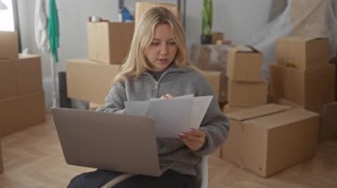 Yeni dairede bir kadın dizüstü bilgisayarla evrakları inceliyor. Etrafı kutular ve boş eşyalar ile çevrili..
